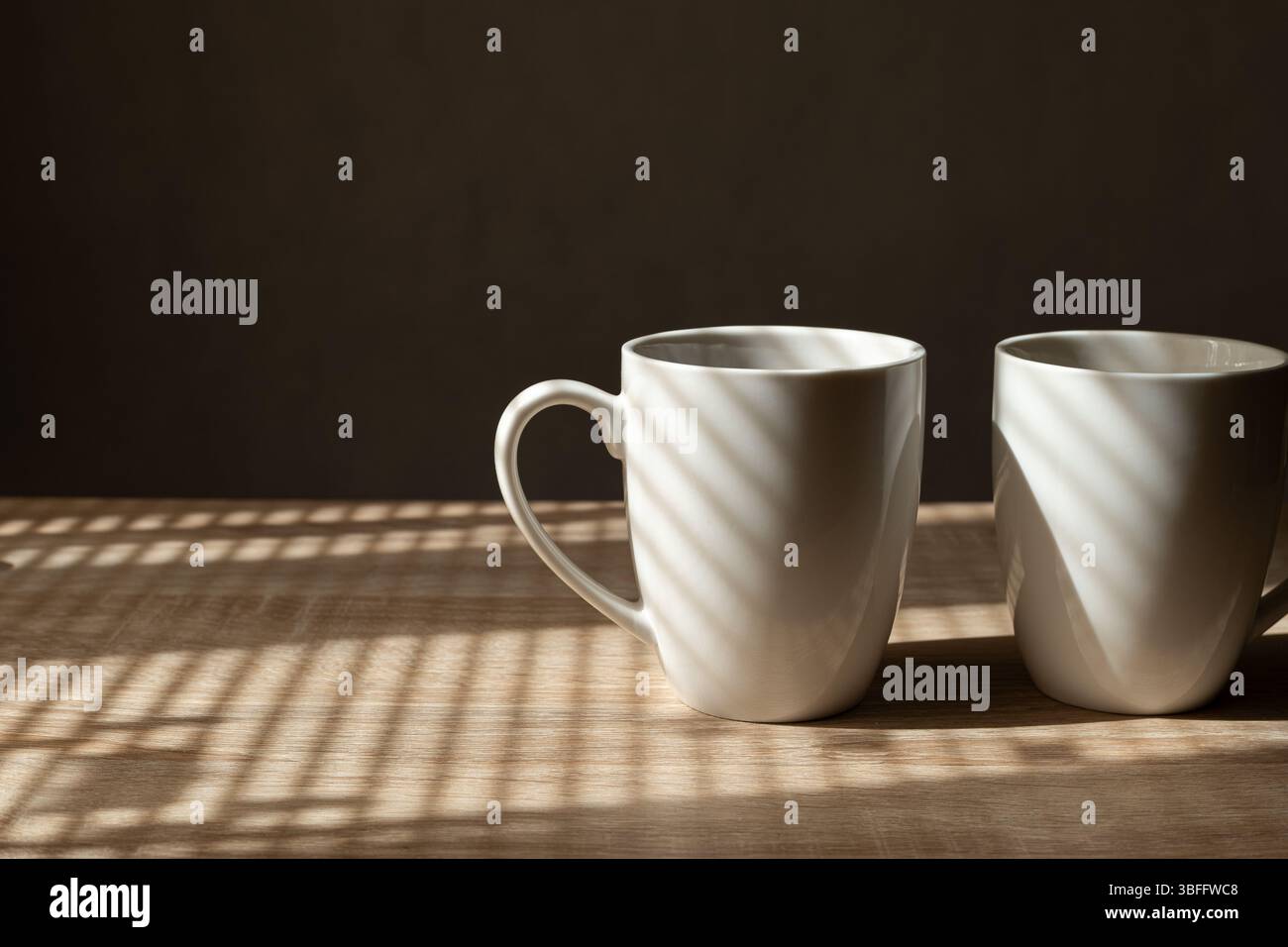 Deux tasses à café sur la table avec éclairage latéral et ombres aveugles de fenêtre Banque D'Images Deux tasses à café sur la table avec éclairage latéral et ombres aveugles de fenêtre Banque D'Images