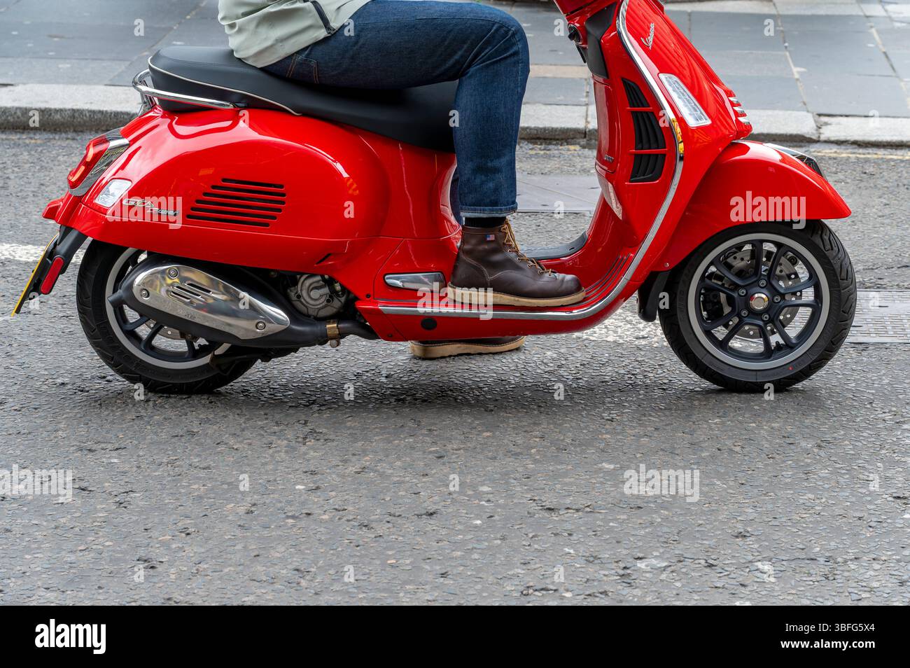 Un homme assis sur un scooter rouge vespa dans une rue de la ville, Royaume-Uni Banque D'Images