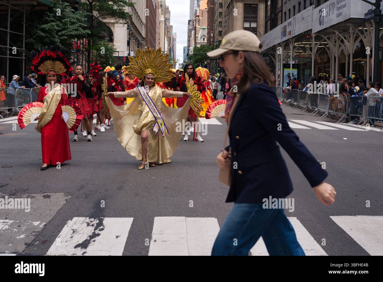 Un défilé d'individus costumés, principalement des femmes, dans des vêtements rouges et or vifs, marche dans une rue de la ville. Une femme dans une robe dorée se tient ou Banque D'Images