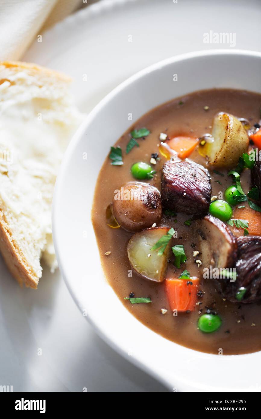 Ragoût de bœuf en morceaux avec petits pois, carottes et pommes de terre dans un bouillon Banque D'Images