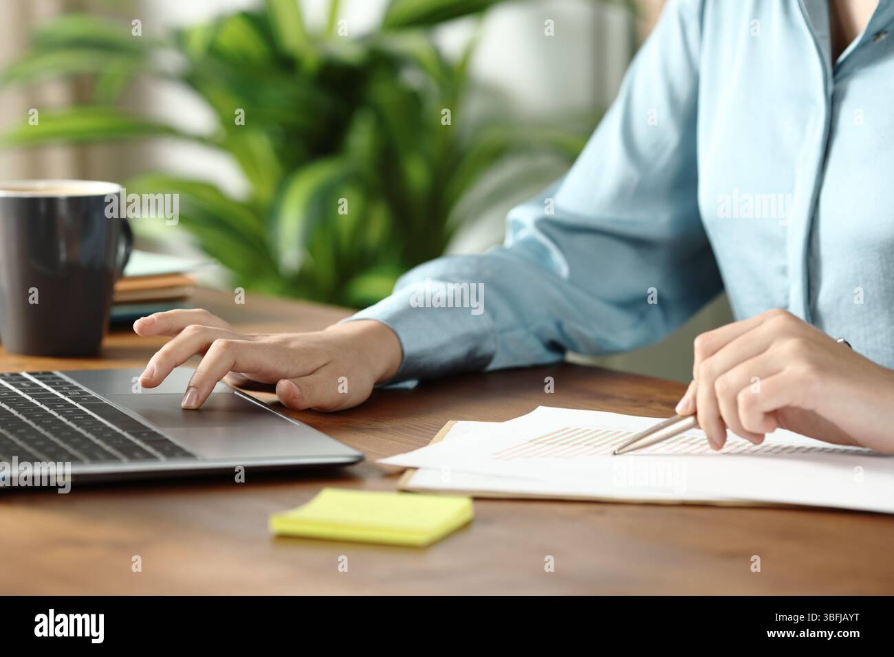 Gros plan d'une main de femme travaillant comparant le document avec le contenu en ligne au bureau Banque D'Images