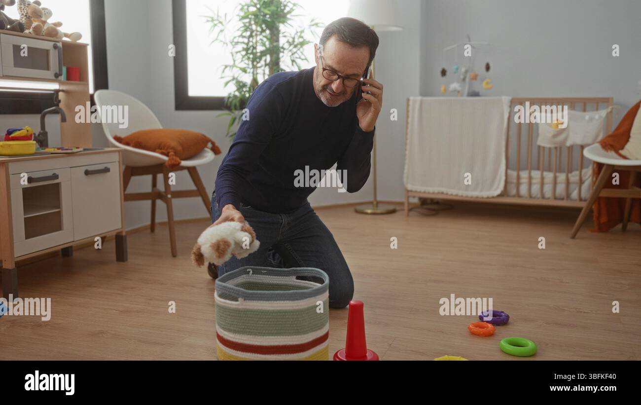 Homme organisant des jouets dans une chambre confortable tout en parlant au téléphone, entouré d'articles de bébé colorés dans un environnement domestique moderne. Banque D'Images