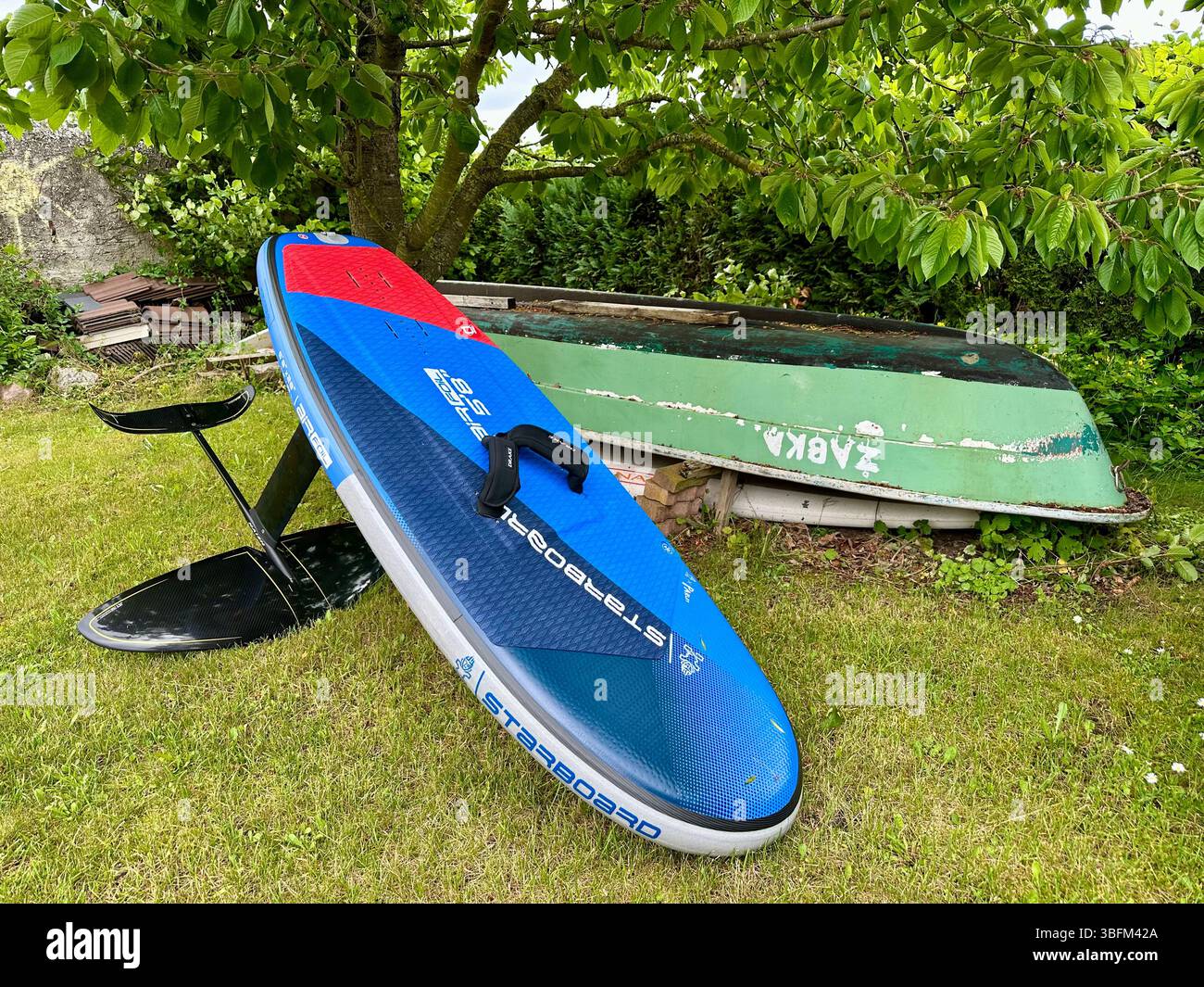 Une planche à paddle gonflable hydroptère dans un jardin à côté d'un vieux bateau ANKA Banque D'Images