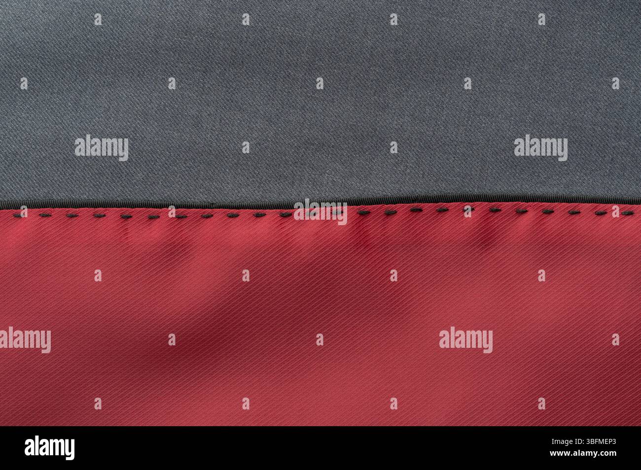 Vue rapprochée d'un textile présentant une section de tissu gris lisse jointe à une section rouge vif présentant des coutures. Banque D'Images