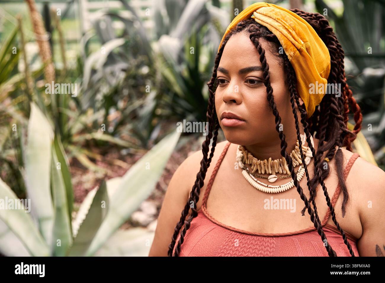 Un moment serein comme une femme noire confiante admire la verdure autour d'elle dans une jolie robe. Banque D'Images