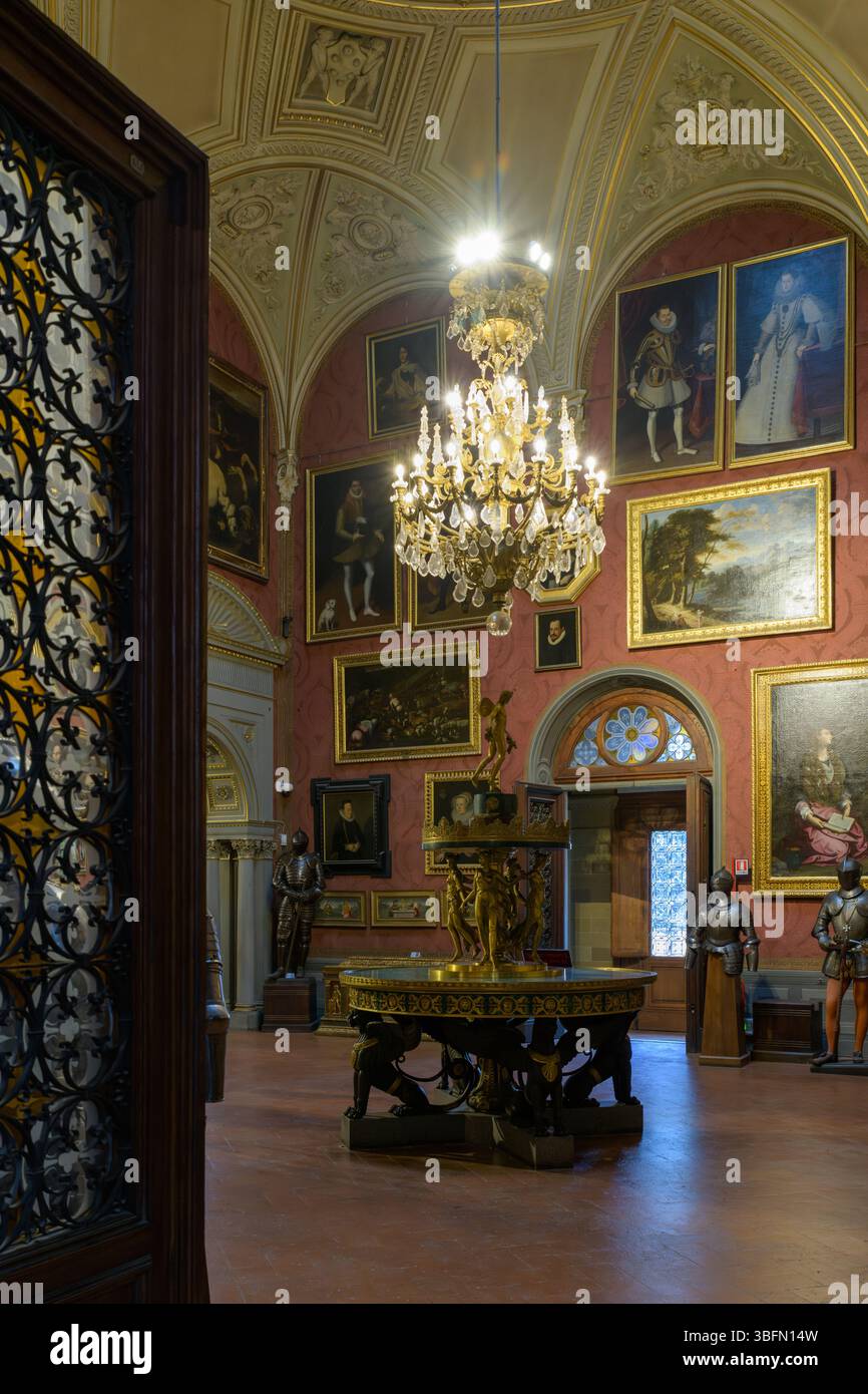 Galerie éclairée par des lustres au Stibbert Museum, Florence, Italie avec des expositions d'armures, des portraits et une fontaine centrale dorée. Banque D'Images