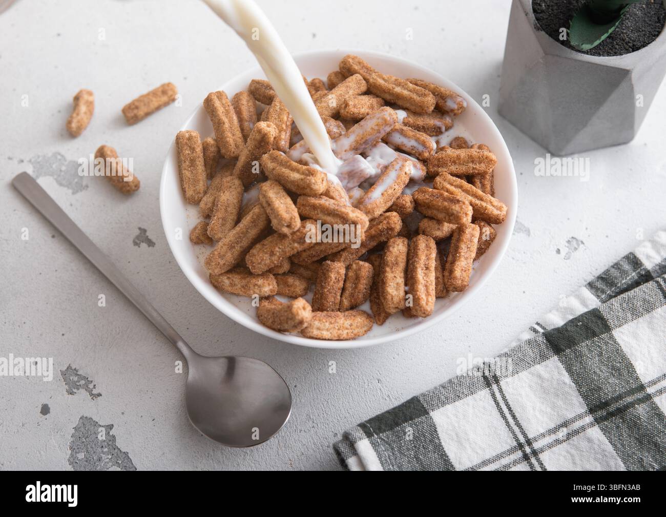 Céréales de petit déjeuner churros sucrés dans une assiette et verser du lait dedans avec une cuillère sur la table. Banque D'Images