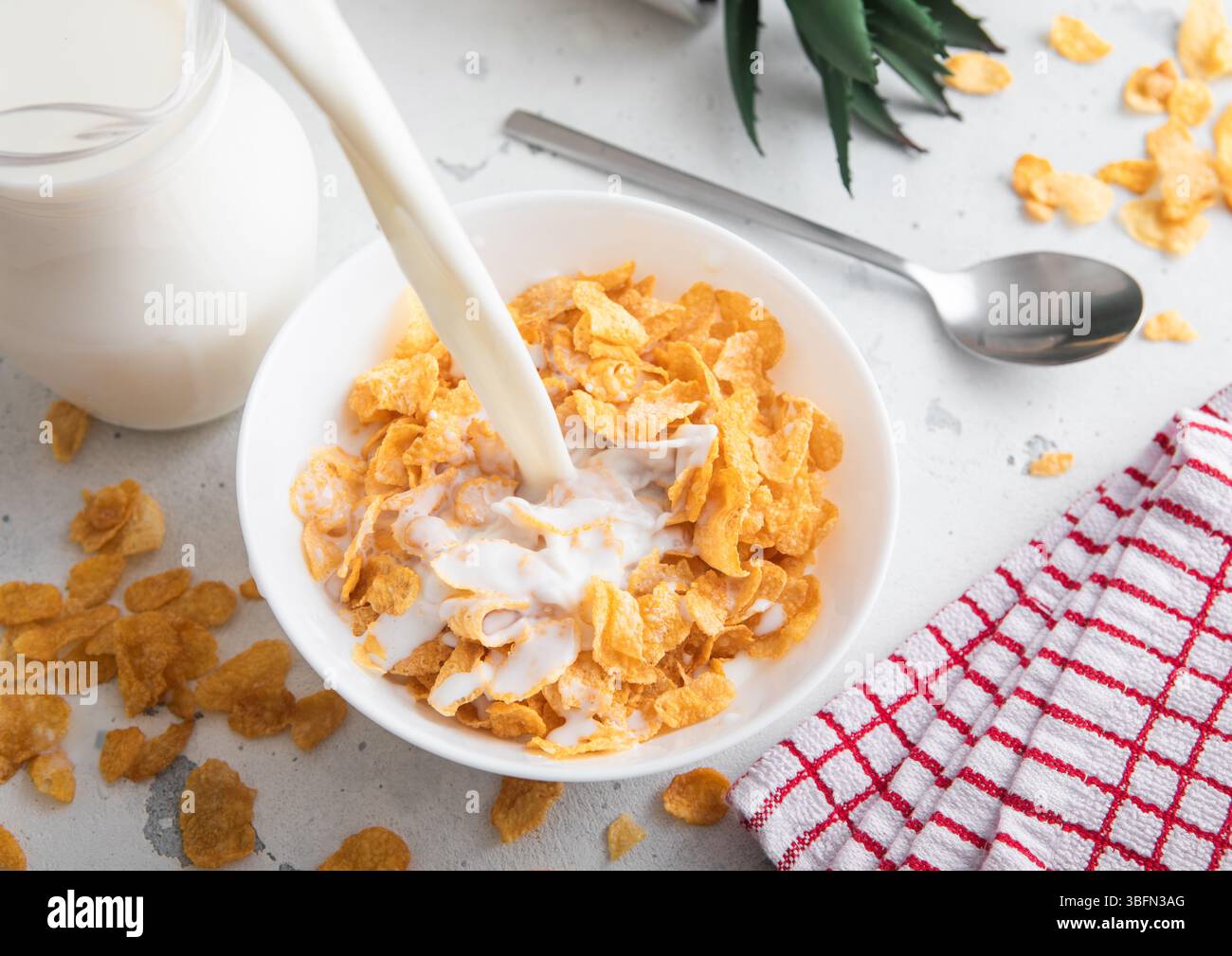 Lait versé dans le bol avec flocons de maïs jaunes originaux céréales de petit déjeuner avec cuillère sur la table. Banque D'Images