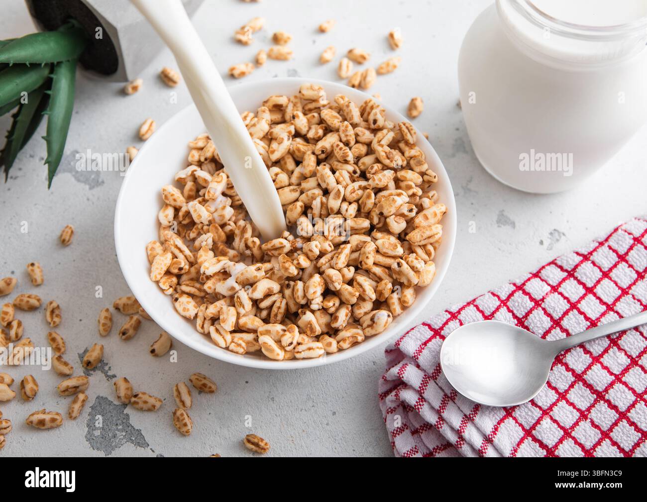 Verser le lait dans le bol avec des krispies de riz au miel petit déjeuner de céréales du matin avec cuillère et serviette de cuisine. Banque D'Images