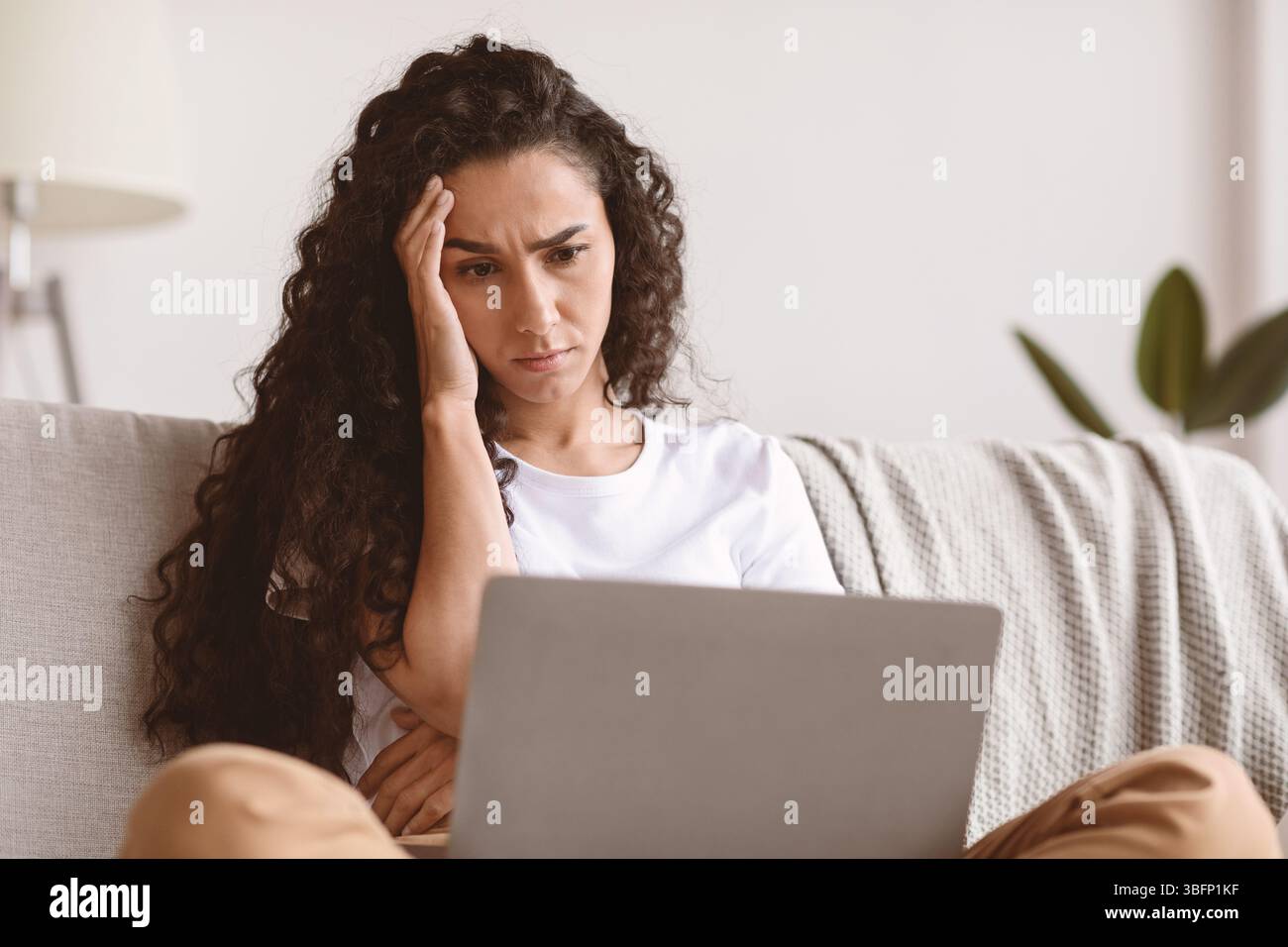Jeune femme troublée assise sur un canapé avec un ordinateur portable, gros plan Banque D'Images