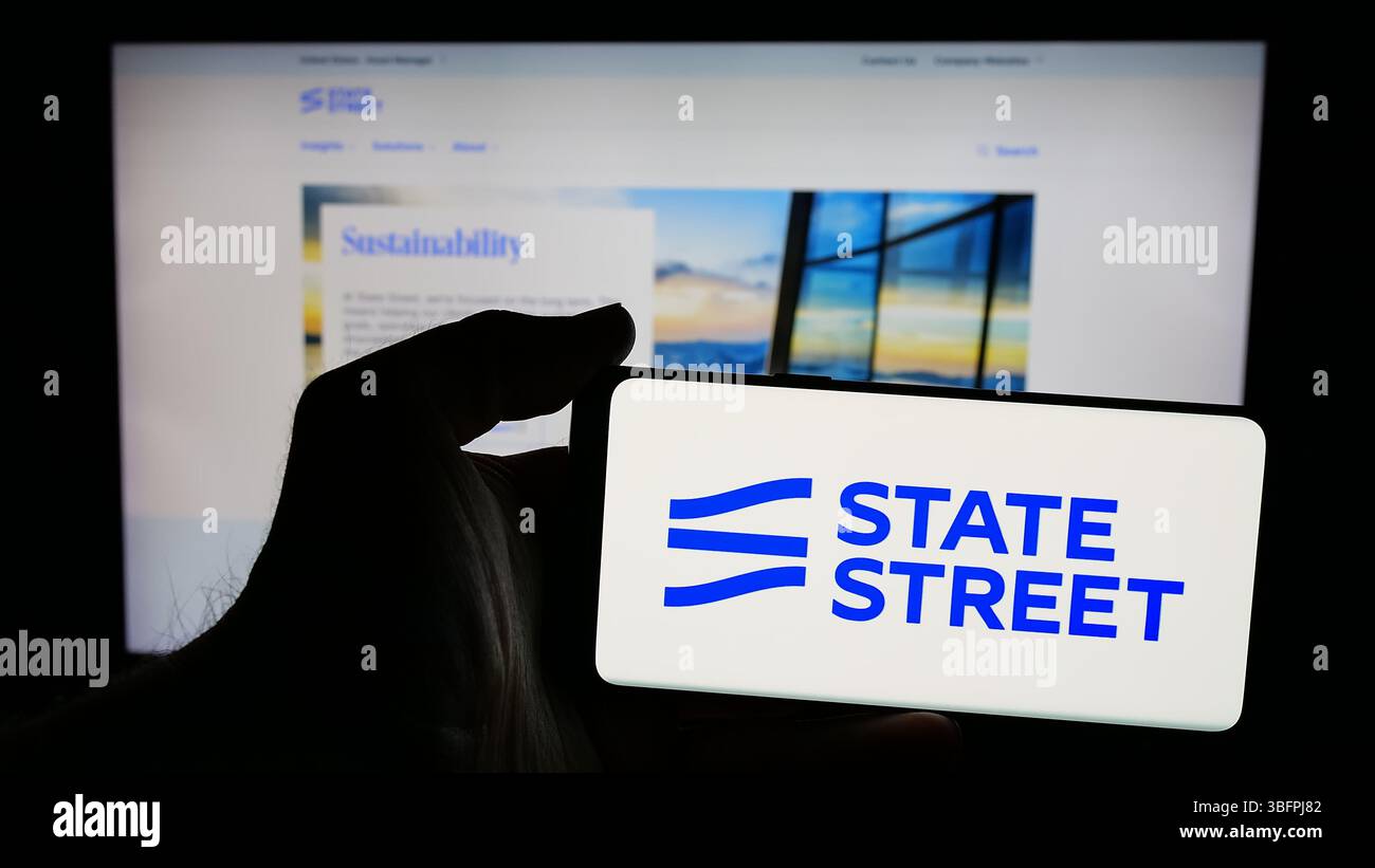 Stuttgart, Allemagne - 01-23-2025 : personne tenant un téléphone portable avec le logo de la société financière américaine State Street Corporation sur l'écran en face de la page Web Banque D'Images Stuttgart, Allemagne - 01-23-2025 : personne tenant un téléphone portable avec le logo de la société financière américaine State Street Corporation sur l'écran en face de la page Web Banque D'Images