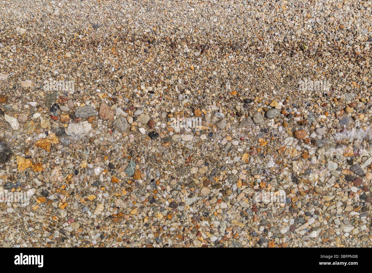 Petits cailloux sur le rivage dans une plage et une petite vague le jour ensoleillé, vu d'en haut. Voyage naturel abstrait, vacances et fond d'été. Banque D'Images