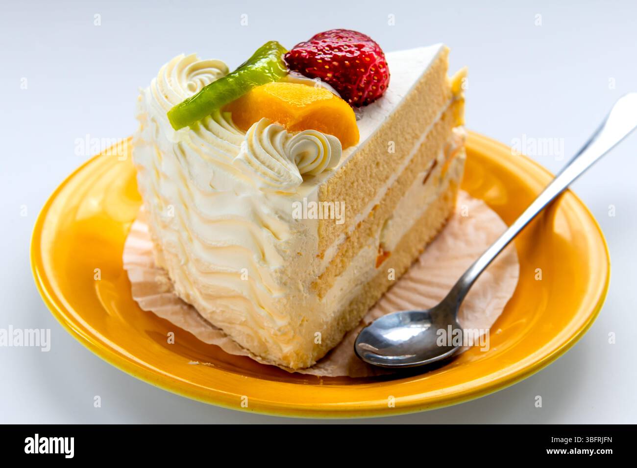 Gros plan d'une tranche de gâteau à la crème de fruits avec fraise, pêche et kiwi isolé sur blanc. Banque D'Images
