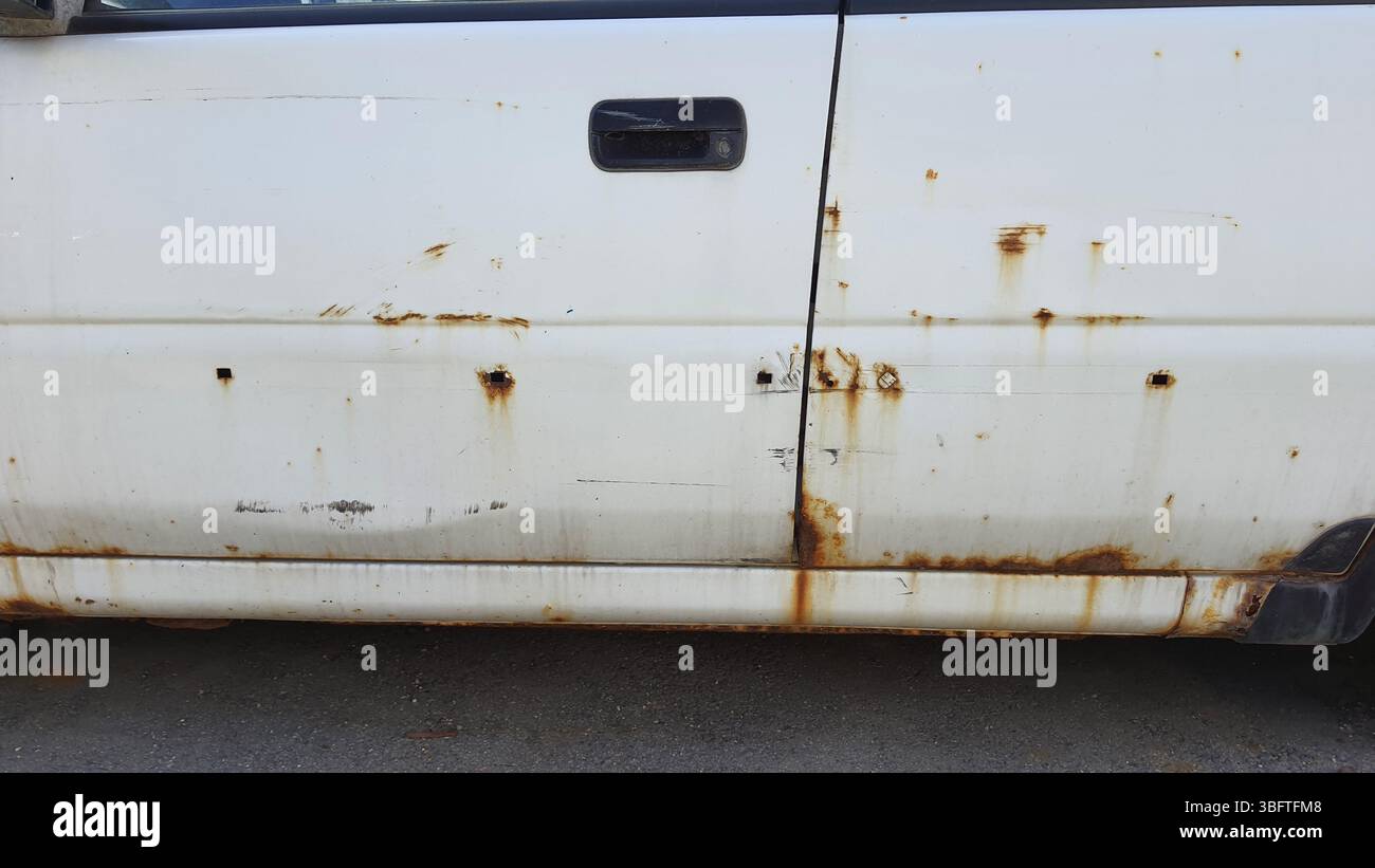 Vue rapprochée d'une porte de voiture blanche rouillée, montrant la corrosion et les dommages visibles, soulignant l'impact du temps et de la négligence sur le véhicule endommagé Banque D'Images