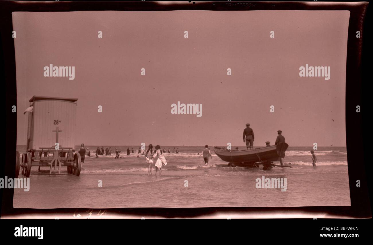 En 1913, plusieurs hommes à bord d'un bateau à roues observent des nageurs au large de la plage de Scheveningen, aux pays-Bas. Cette photo a été prise lors de la tournée européenne de la famille Arras, offrant un aperçu de la vie balnéaire néerlandaise du début du XXe siècle. Scheveningen est une station balnéaire populaire aux pays-Bas. Banque D'Images