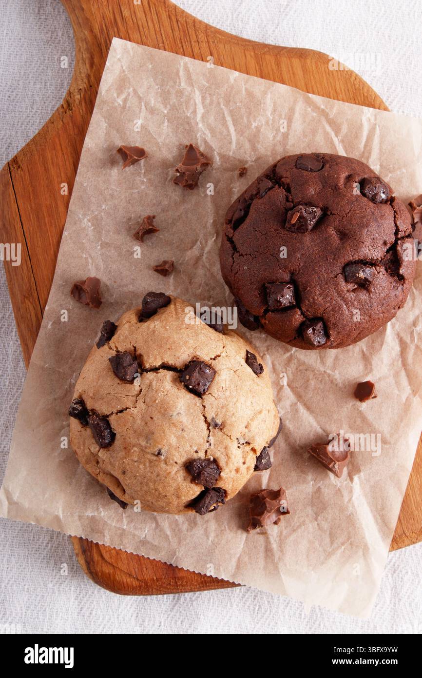 deux biscuits aux pépites de chocolat sur papier parchemin, pâte claire et foncée, planche de bois, vue de dessus Banque D'Images