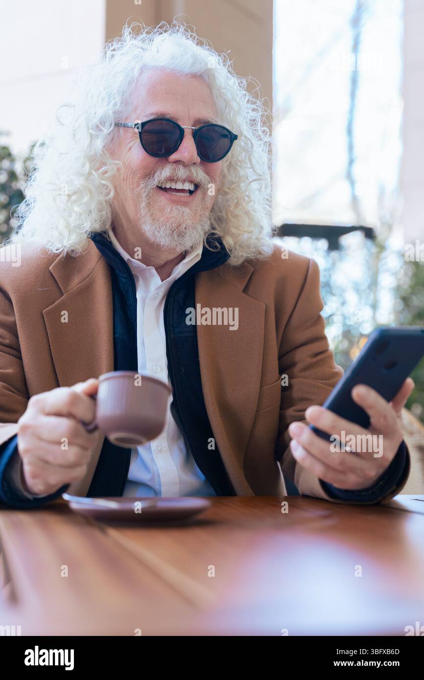 Portrait vertical de l'homme senior avec du café à l'aide d'un smartphone au café extérieur Banque D'Images