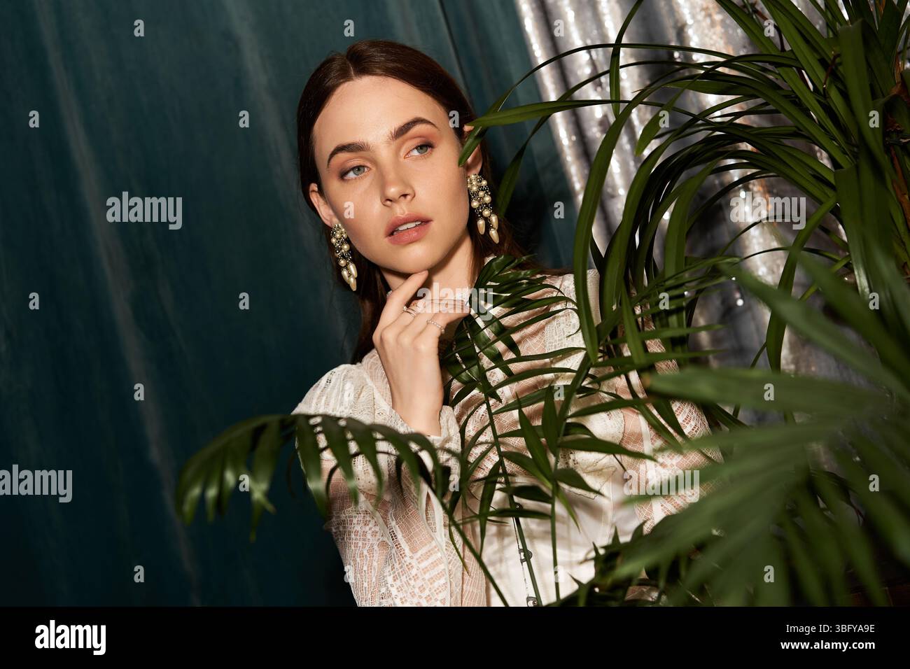 Belle jeune femme célèbre la mode vintage entourée de plantes riches et d'une lumière douce. Banque D'Images
