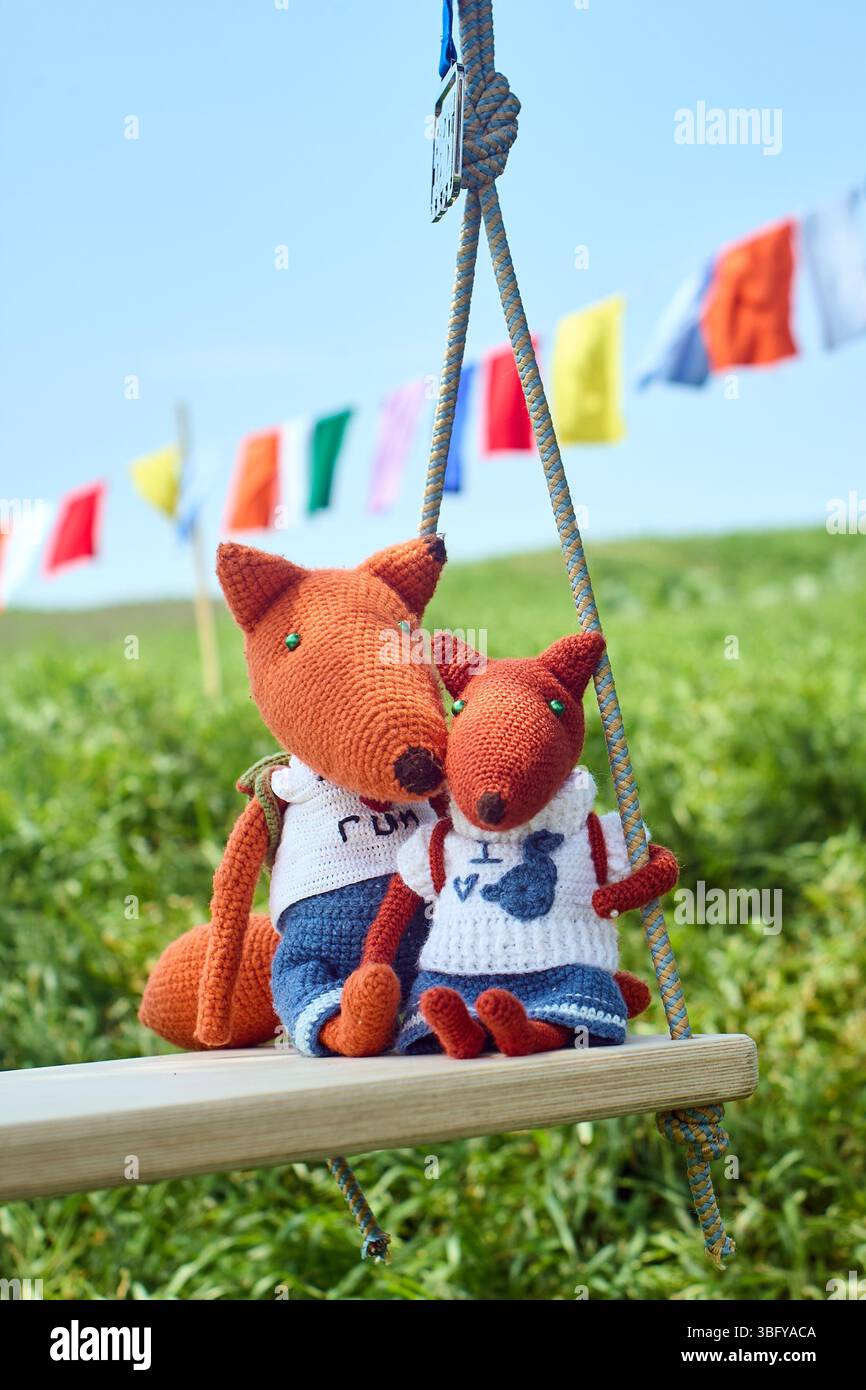 Deux jouets de renard crochetés, habillés de vêtements et avec des sacs à dos, chevauchant sur une balançoire. Jouets pour enfants, faits à la main Banque D'Images