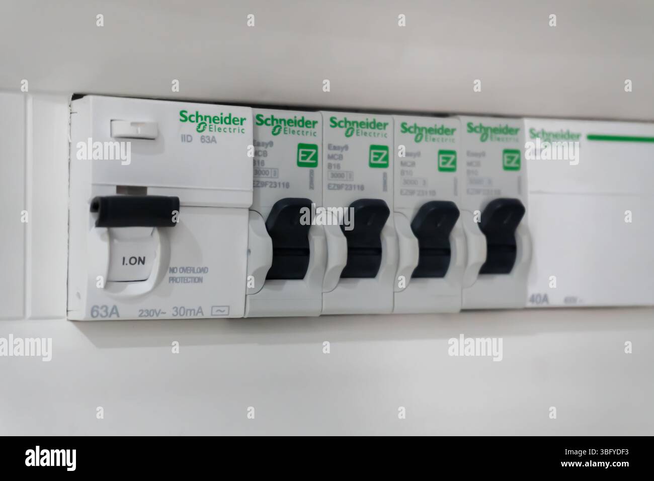 Vue rapprochée d'un consommateur électrique moderne ou d'une boîte à fusibles, avec une rangée de disjoncteurs électriques Schneider blancs avec interrupteurs noirs Banque D'Images