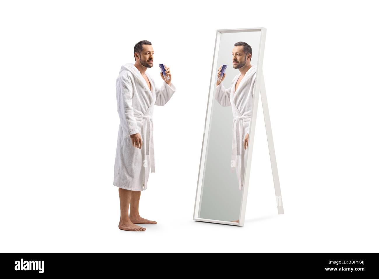 Jeune homme dans un peignoir pulvérisant un parfum devant un miroir isolé sur fond blanc Banque D'Images Jeune homme dans un peignoir pulvérisant un parfum devant un miroir isolé sur fond blanc Banque D'Images