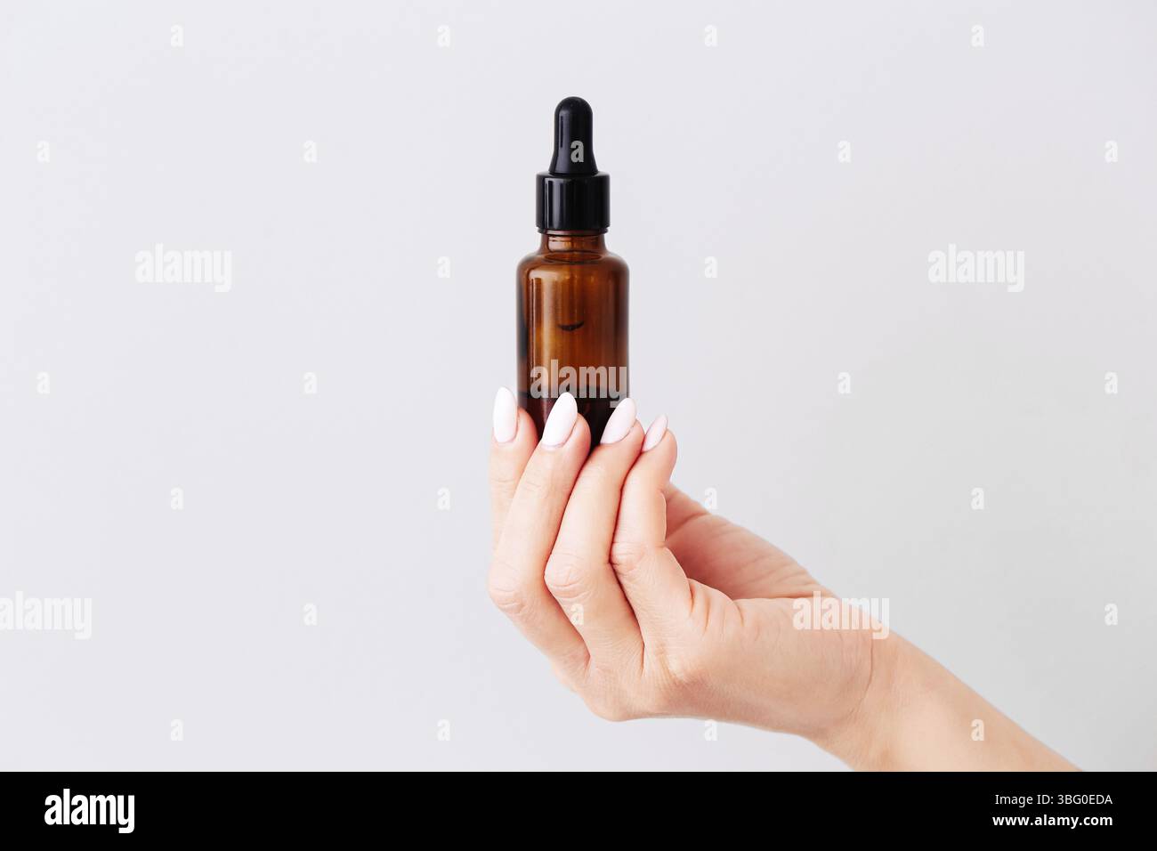 Flacon compte-gouttes marron. Récipient pour huile cosmétique tenant la main d'une femme. Concept minimaliste de produit de soin de la peau. Emballage d'essence de beauté biologique. Banque D'Images