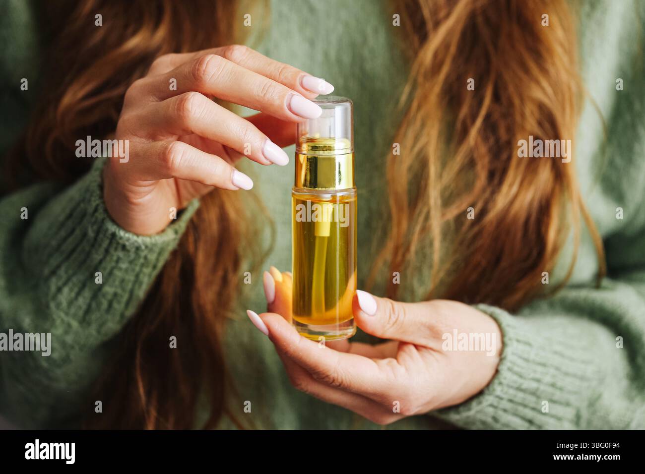 Huile d'argan dans une bouteille en verre. Femme tenant le sérum cosmétique doré. Concept de cheveux naturels et de soins de la peau. Mains douces avec manucure. Produit de beauté et de bien-être. Banque D'Images