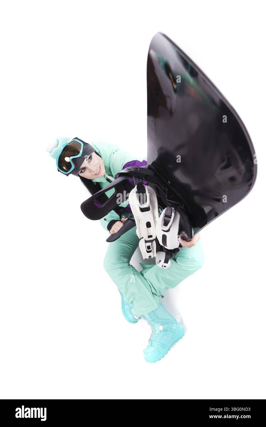 Image verticale, isolée sur blanc, jolie femme caucasienne en tenue de ski violette, lunettes de ski bleues et pantalon bleu assis jambes croisées et tenir bla Banque D'Images