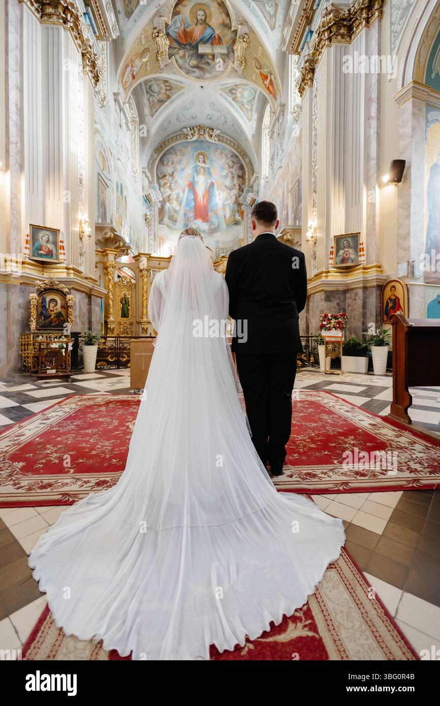 Vue arrière de mariée élégante et mariée debout dans la belle église pendant la cérémonie de mariage traditionnelle Banque D'Images