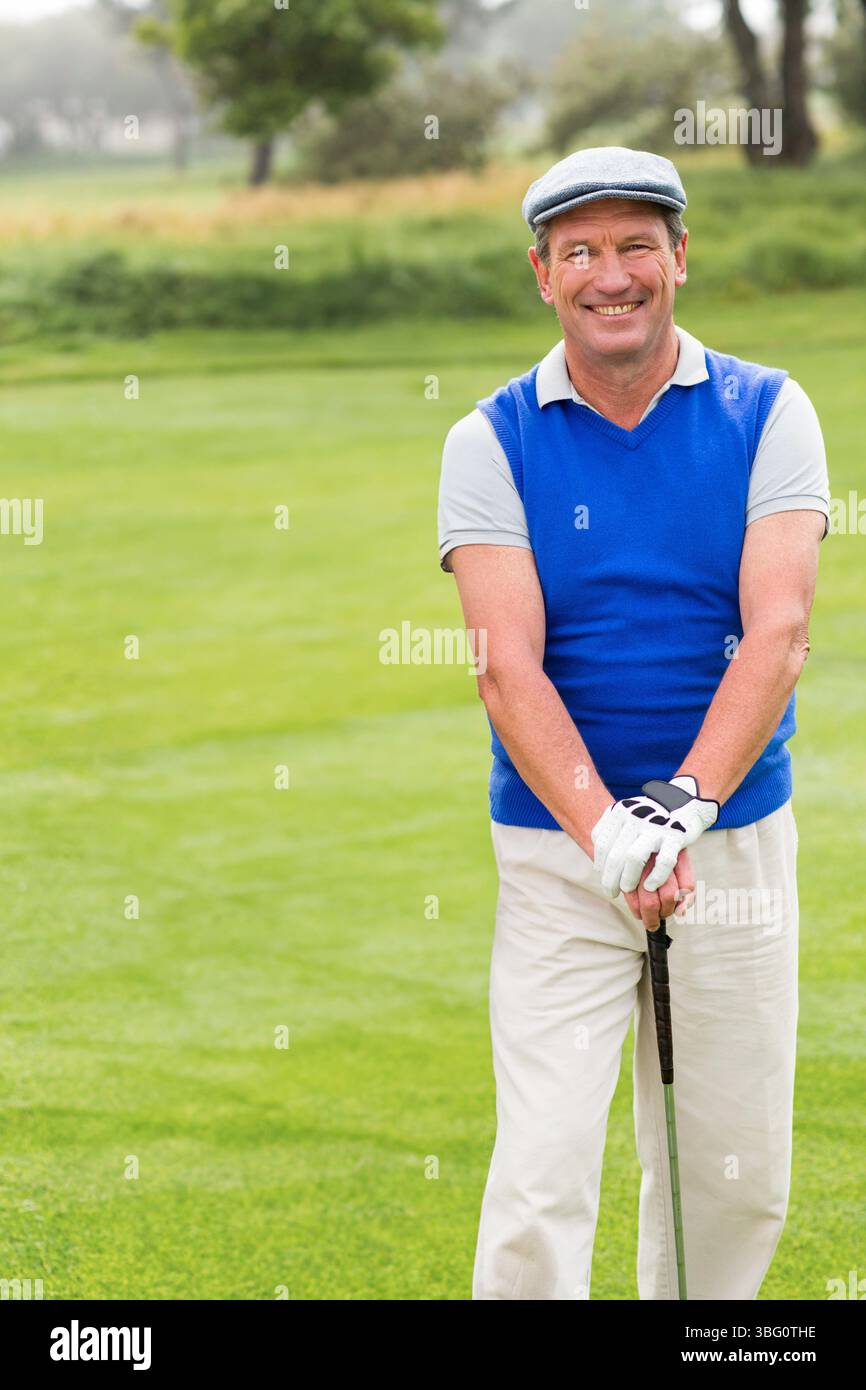 Golfeur afro-américain senior tenant un club avec des mains gantées souriant sur le fairway portant une casquette plate Banque D'Images