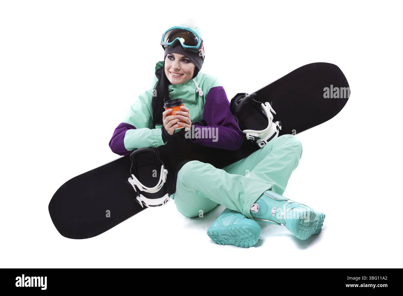 Image verticale, isolée sur blanc, jolie femme caucasienne en tenue de ski violette, lunettes de ski bleues et pantalon bleu assis jambes croisées et tenir bla Banque D'Images