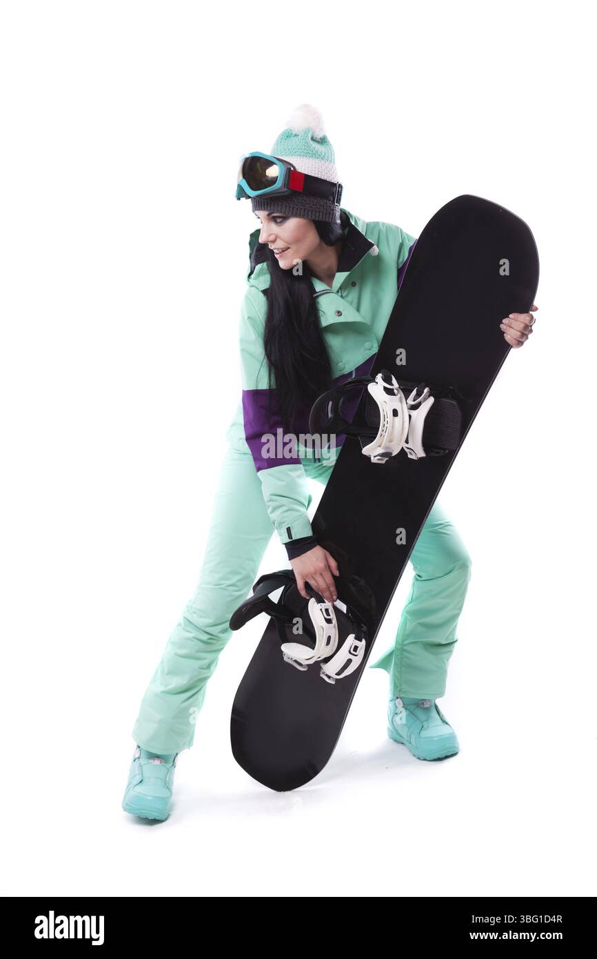 Image verticale, isolée sur blanc, jolie femme caucasienne en tenue de ski violette, lunettes de ski bleues et pantalon bleu tiennent le snowboard noir, jambes ap Banque D'Images