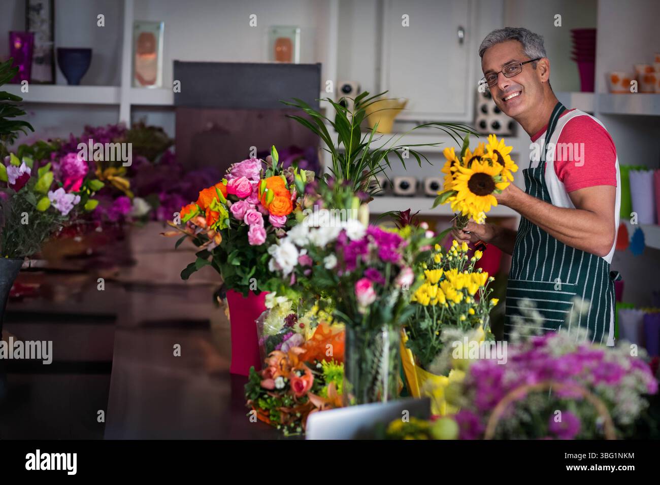 Fleuriste masculin adulte moyen portant tablier arrangeant des bouquets sur le comptoir à la boutique de fleurs, espace copie Banque D'Images