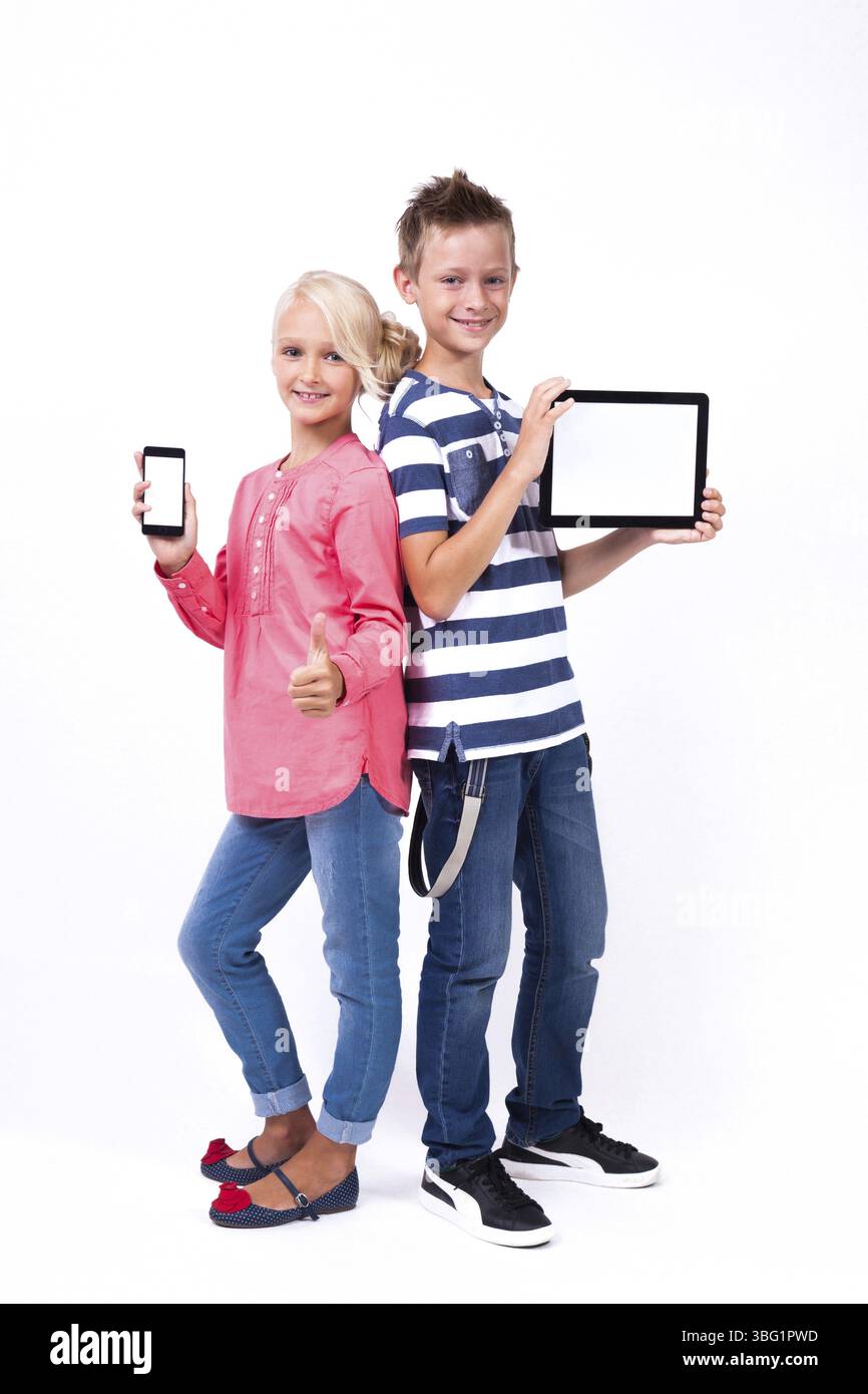 Les écoliers souriants apprennent à connaître le monde et communiquent à l'aide de tablettes et de téléphones modernes, une formation intéressante et la communication gad Banque D'Images