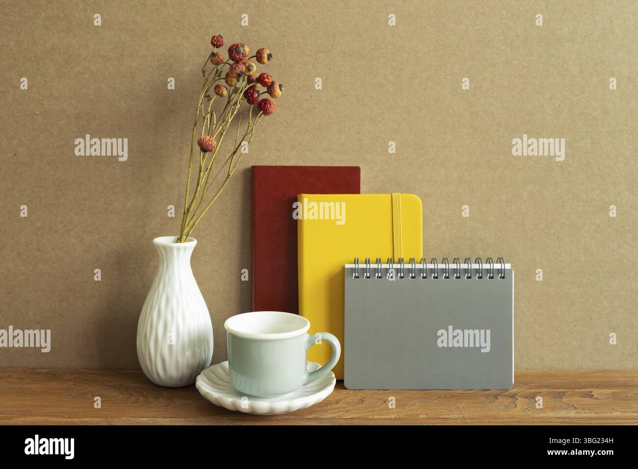Carnet, tasse à café, fleur sèche sur bureau en bois. Fond de mur brun. Espace de travail Banque D'Images