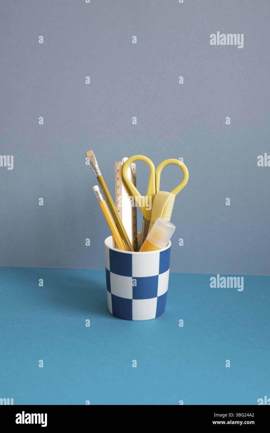 Crayon jaune, règle, surligneur, ciseaux dans support sur bureau bleu Banque D'Images