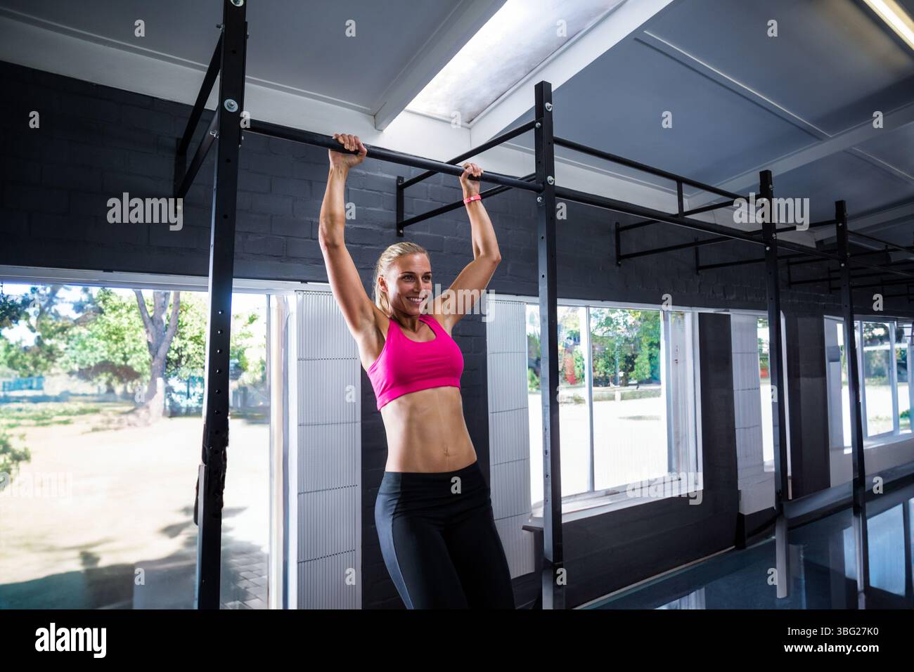 Femme en soutien-gorge de sport rose et leggings noirs effectuant un pull-up sur barre horizontale dans la salle de gym Banque D'Images