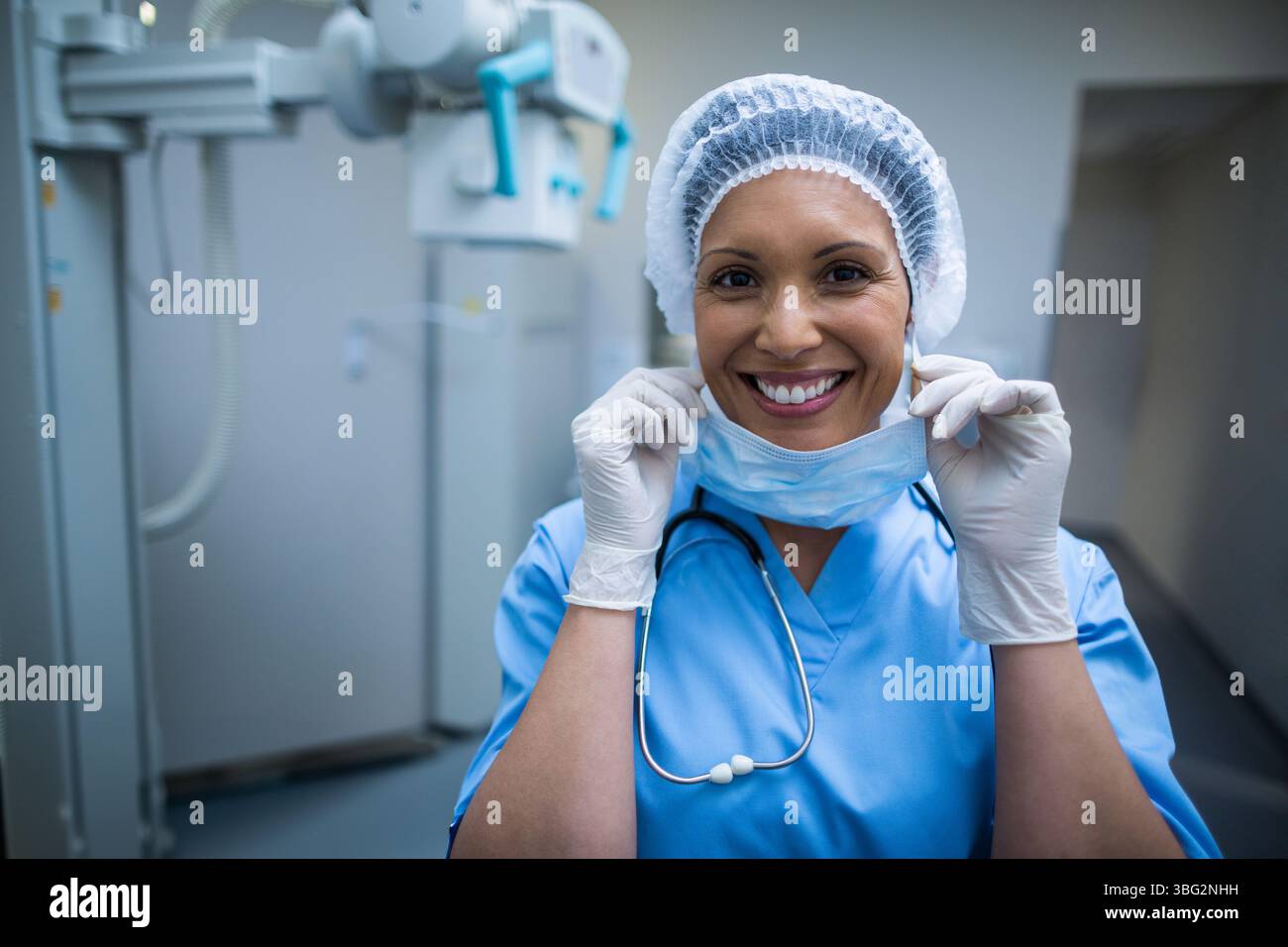 Infirmière tirant le masque chirurgical avec les mains gantées dans une salle de radiologie avec appareil de radiologie Banque D'Images