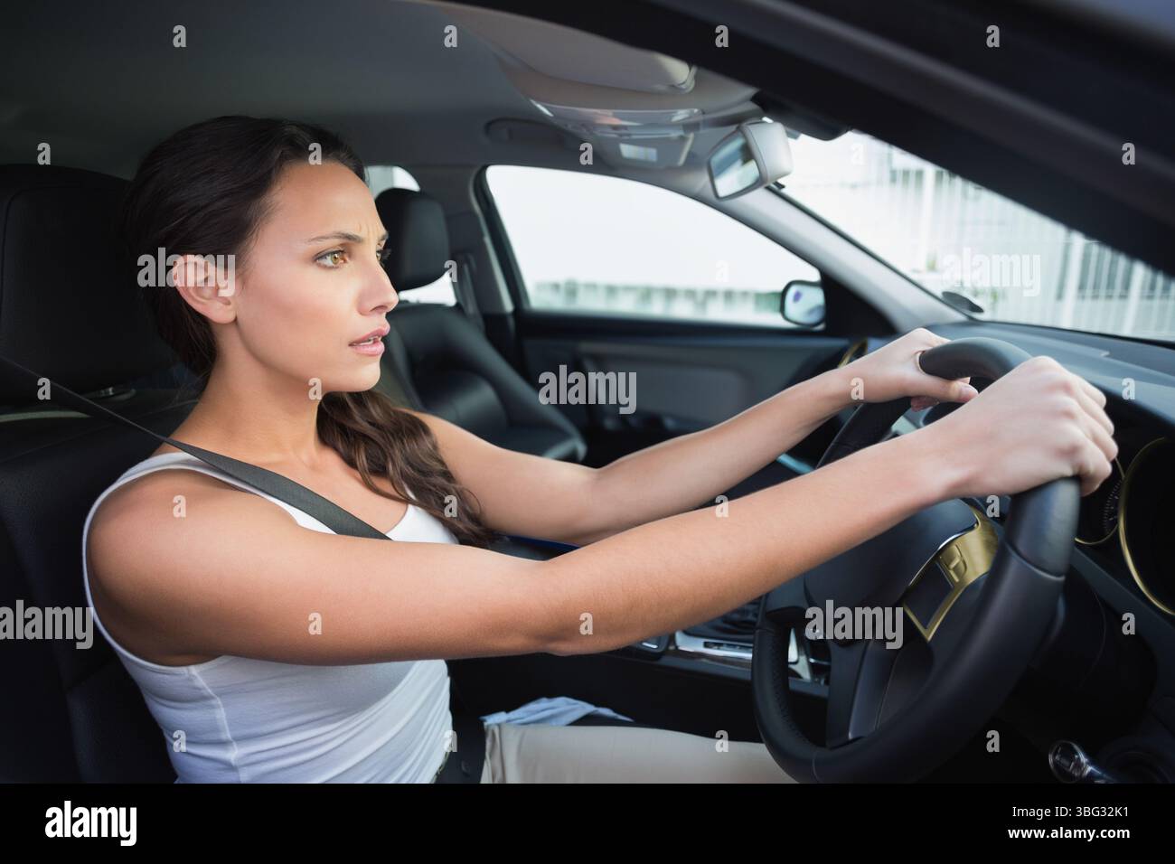 Femme attachant la ceinture de sécurité tout en saisissant le volant et en se concentrant sur le tableau de bord à l'intérieur de la cabine de voiture Banque D'Images