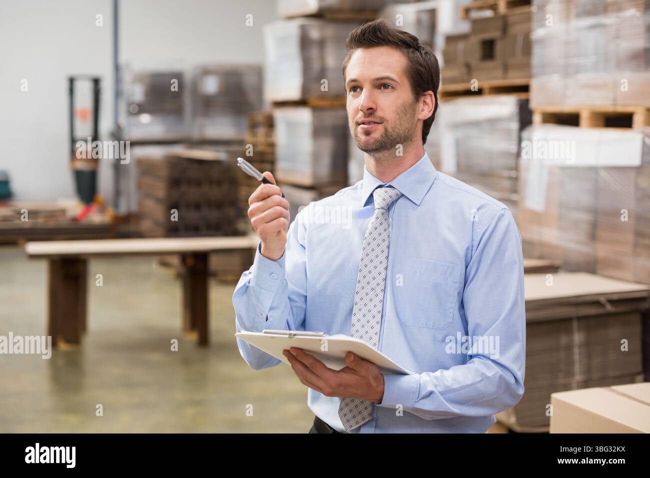 Homme dans la trentaine debout près de la table de palette inspectant les marchandises sur le presse-papiers dans l'entrepôt, espace de copie Banque D'Images