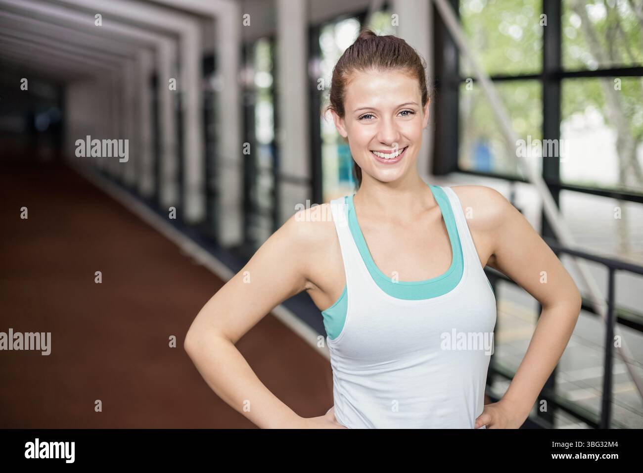 Femme debout sur la piste portant un débardeur souriant par des poutres et des balustrades près des fenêtres, espace de copie Banque D'Images