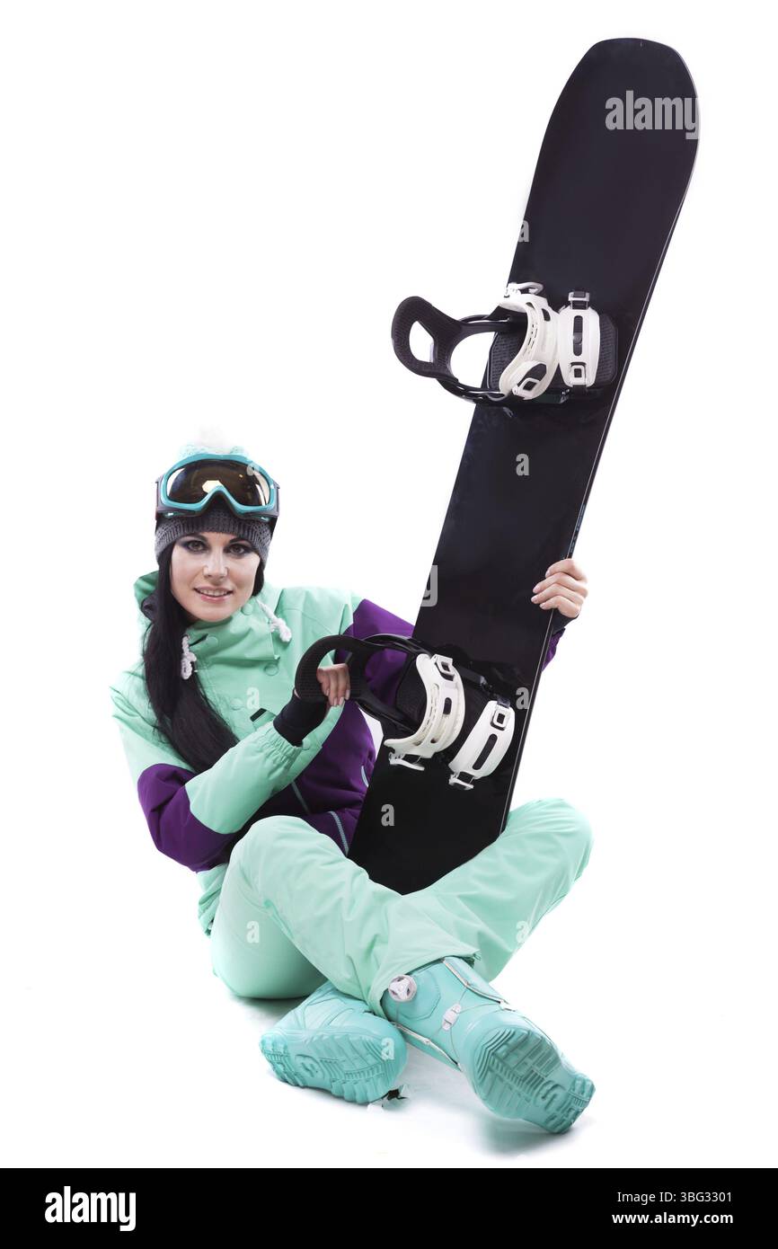 Image verticale, isolée sur blanc, jolie femme caucasienne en tenue de ski violette, lunettes de ski bleues et pantalon bleu assis jambes croisées et tenir bla Banque D'Images