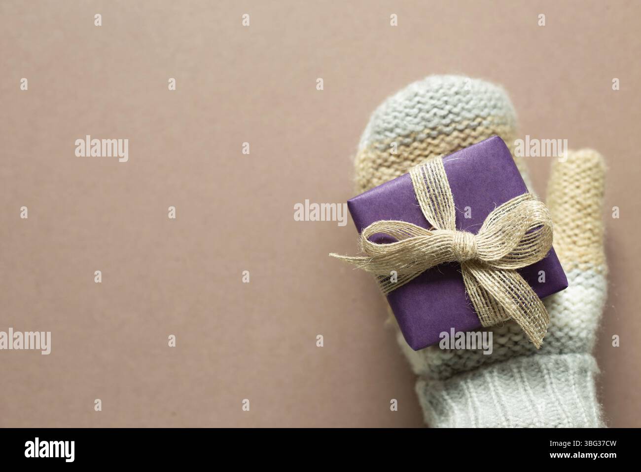 Gants tricotés hiver main avec boîte cadeau violette sur fond marron. Anniversaire, noël, concept de salutation. Vue du dessus, espace copie Banque D'Images