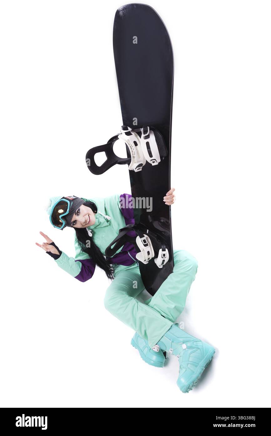 Image verticale, isolée sur blanc, jolie femme caucasienne en tenue de ski violette, lunettes de ski bleues et pantalon bleu assis jambes croisées et tenir bla Banque D'Images