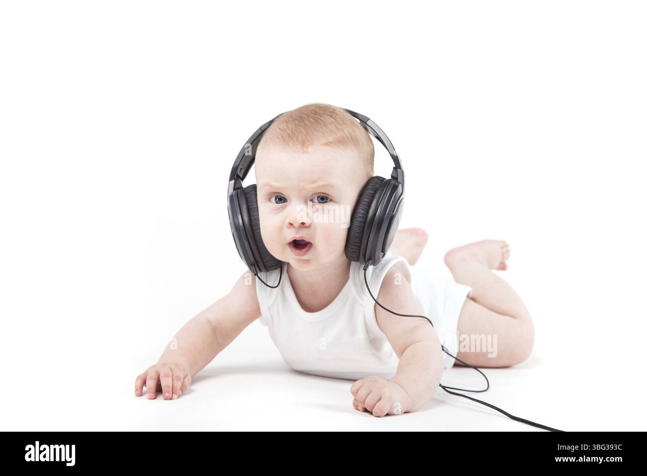 Isolé sur blanc, bébé sérieux garçon caucasien en chemise blanche se trouve avec des écouteurs sur la tête Banque D'Images