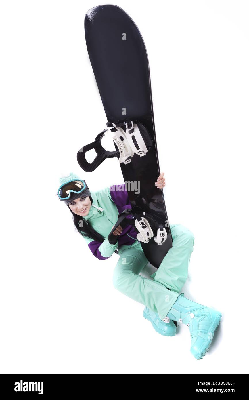 Image verticale, isolée sur blanc, jolie femme caucasienne en tenue de ski violette, lunettes de ski bleues et pantalon bleu assis jambes croisées et tenir bla Banque D'Images
