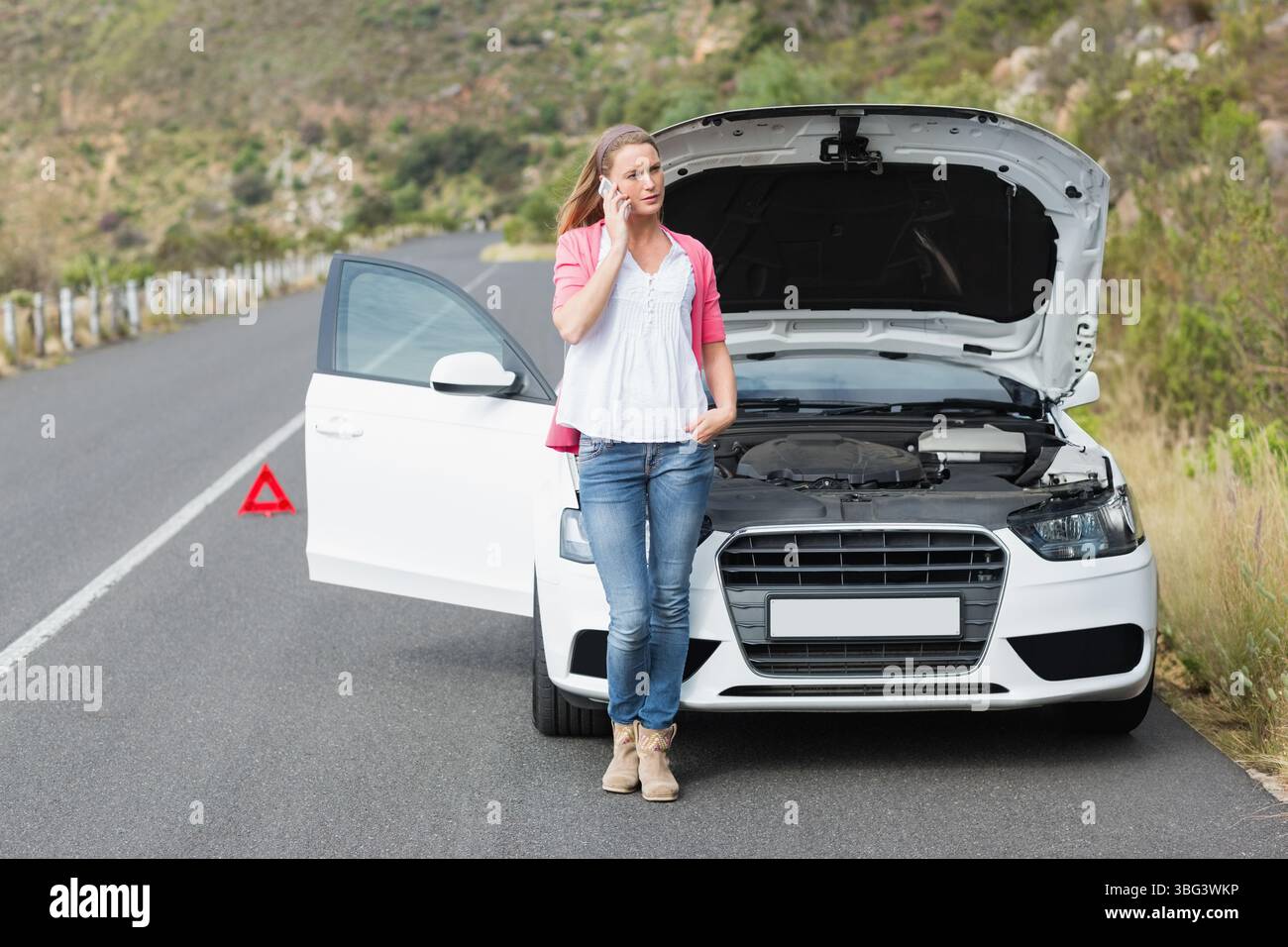 Femme appuyée contre le capot de berline ouvert sur la route de montagne plaçant triangle rouge appelant sur smartphone Banque D'Images