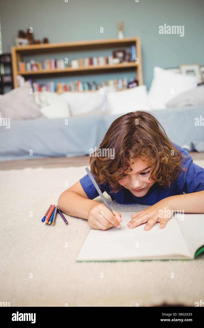 Garçon dessin dans carnet de croquis ouvert sur tapis beige par canapé dans le salon avec des crayons de couleur Banque D'Images