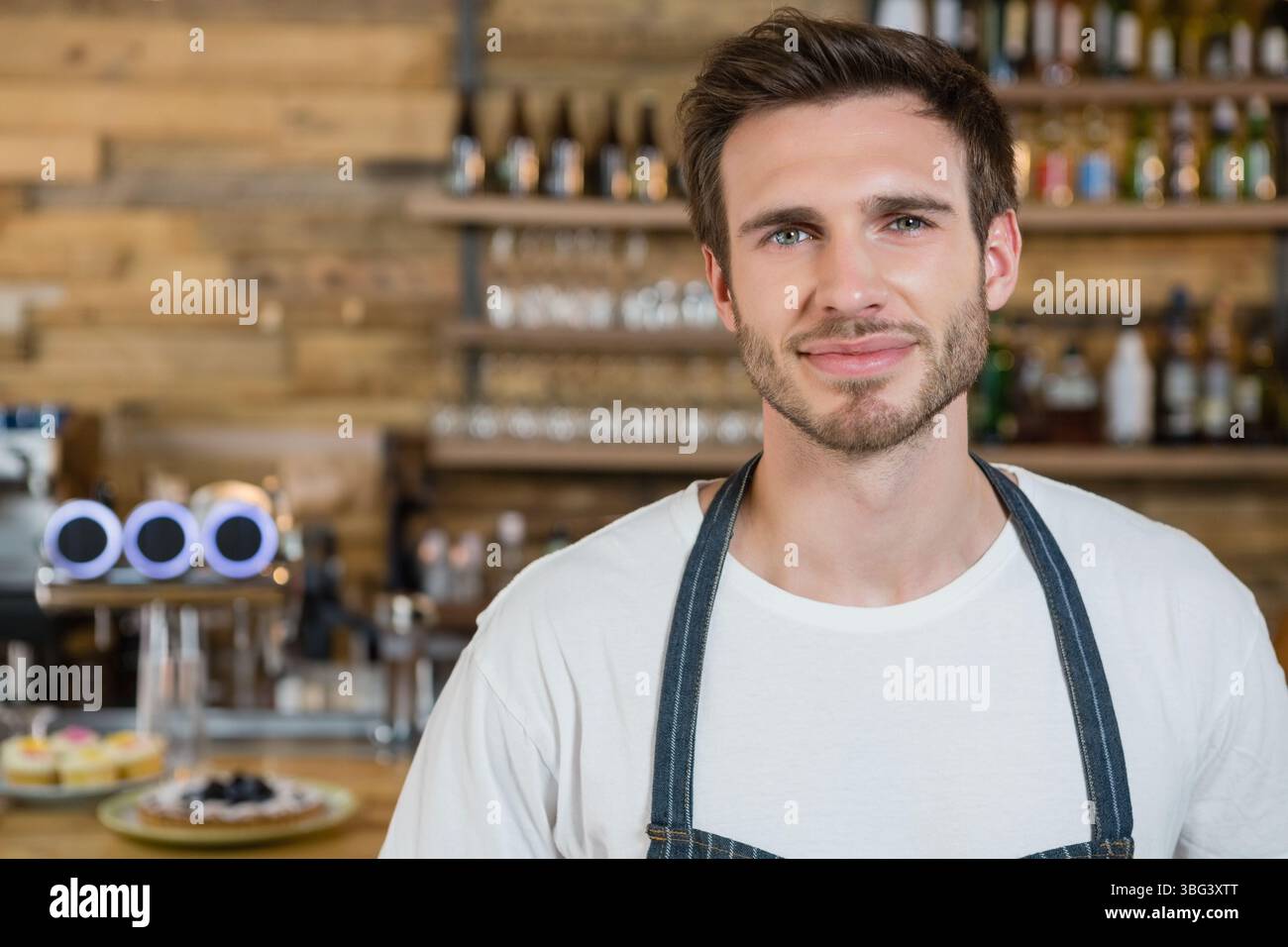 Barman masculin portant un tablier en Jean manipulant le robinet de bière et les pâtisseries derrière le bar, espace de copie Banque D'Images