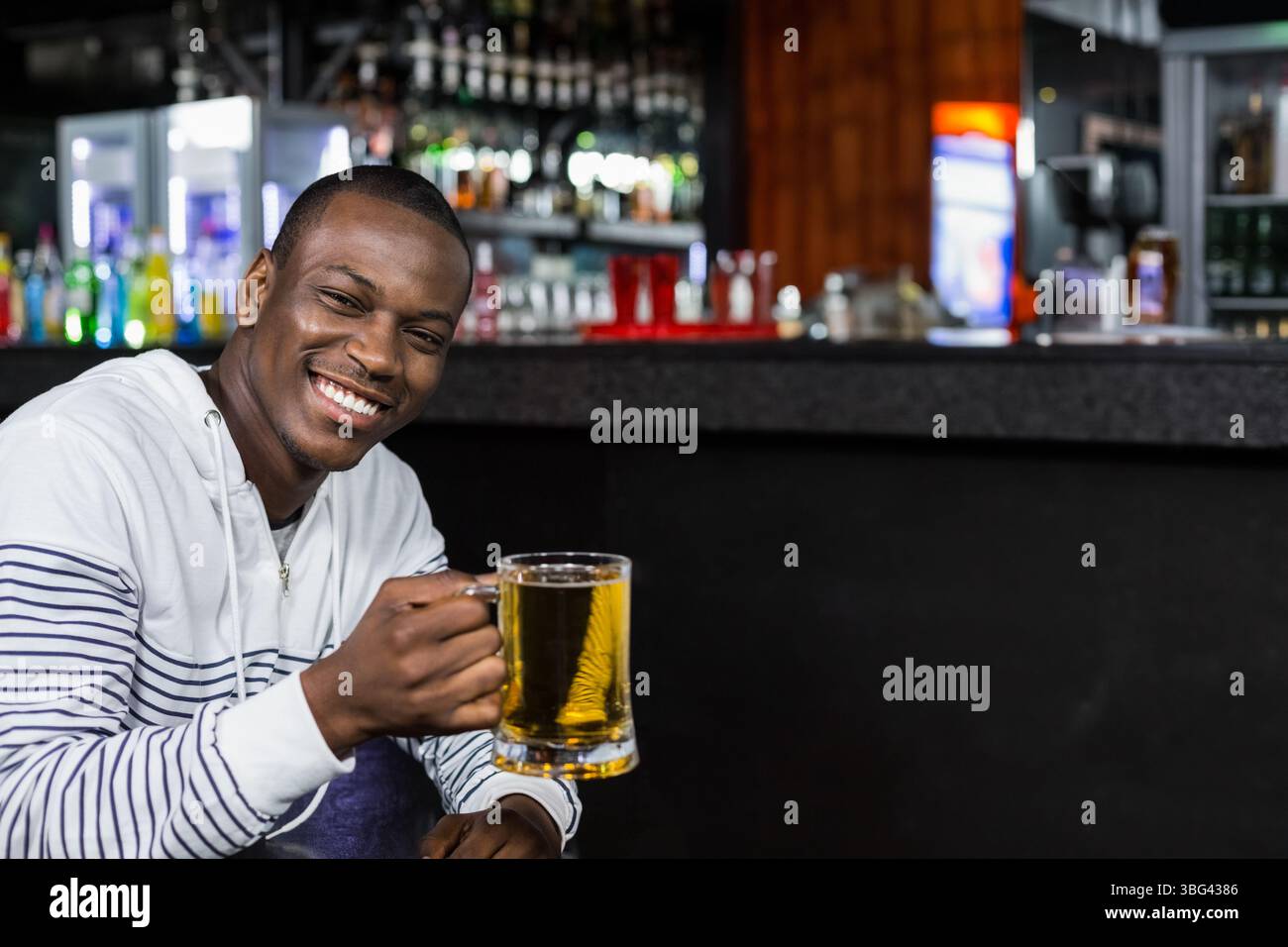 Homme afro-américain portant un sweat à capuche blanc assis au comptoir du pub tenant une tasse de bière claire, espace de copie Banque D'Images Homme afro-américain portant un sweat à capuche blanc assis au comptoir du pub tenant une tasse de bière claire, espace de copie Banque D'Images
